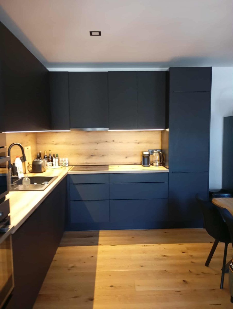 Čierna matná kuchyňa do L s dubovou zástenou a LED svetlom pod hornými skrinkami