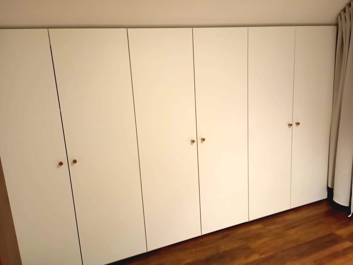 Rad bielych skríň s drevenými úchytkami v podkrovnej izbe